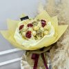 sejambak coklat ferrero rocher dipadankan dengan mawar bergemerlapan emas dan merah, disusun dalam balutan krim untuk persembahan perayaan yang elegan.