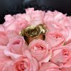 中央に金色のバラが輝くピンクのバラの魅力的なブーケが、黒い紙に包まれ、白いレースのリボンで仕上げられ、エプロンをつけた人から贈られている。