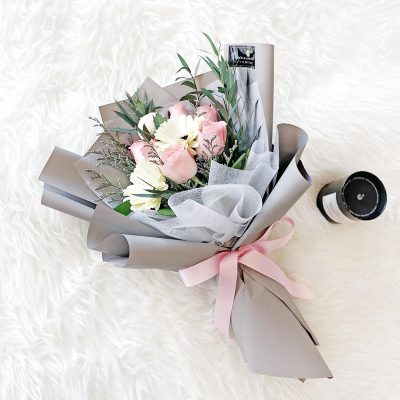 bouquet of pink roses, white gerberas, chrysanthemum ping pong and green leaves in a grey wrapper.