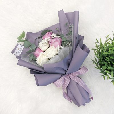 bouquet of purple roses, white roses, baby’s breath and green leaves in a purple wrapper.