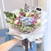 bouquet of blue hydrangea, purple roses, white eustoma, bunny tails and baby’s breath wrapped in white wrapper with ribbon.