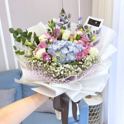 bouquet of blue hydrangea, purple roses, white eustoma, bunny tails and baby’s breath wrapped in white wrapper with ribbon.