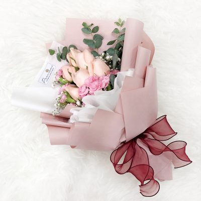 bouquet of pink roses, carnation sprays, baby’s breath and eucalyptus in dusty pink and white wrapper with wine red ribbon.
