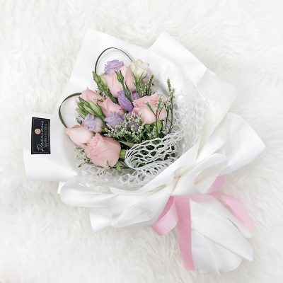 bouquet of pink roses and lilac eustoma with fillers wrapped in white wrapper and pink ribbon.