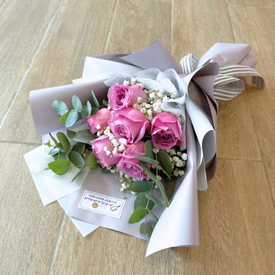 bouquet of purple roses with baby’s breath and eucalyptus wrapped in grey with striped ribbon.