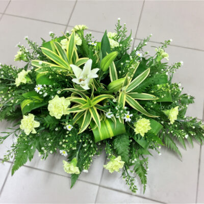 long and low casket flower featuring casablanca lily with green carnation and lush greenery arranged horizontally.