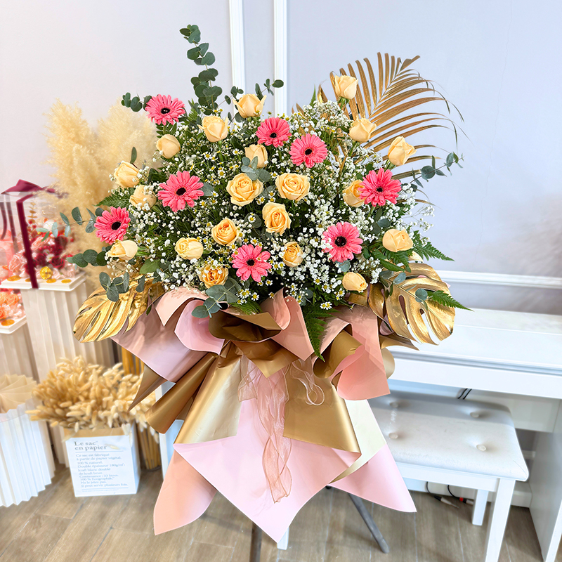 opening flower stand featuring champagne roses and pink gerberas with baby's breath and chamomile wrapped in soft pink and gold paper