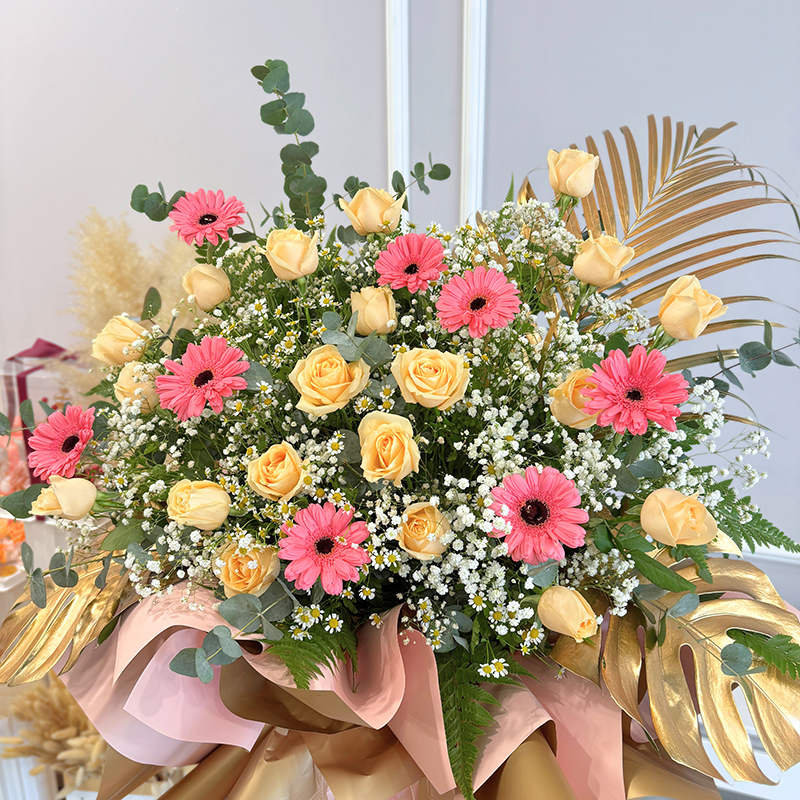 a tall congratulation flower stand with a mix of pink gerberas and champagne roses accented by delicate baby's breath and chamomile