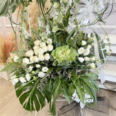 a tall funeral flower bouquet stand with clusters of white rose and eustoma, bright sunflower, and green foliage arranged elegantly