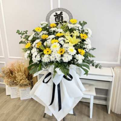 funeral flower stand with yellow gerbera, white chrysanthemum pompom and conca d'or lily wrapped in white with black ribbon