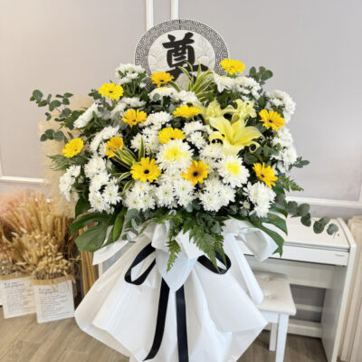 a funeral flower featuring chrysanthemum, yellow gerbera and conca d'or lily on a white wrapped stand