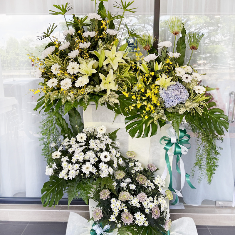 funeral flower stand featuring white lilies, chrysanthemums, hydrangea, and lush green leaves with decorative ribbons