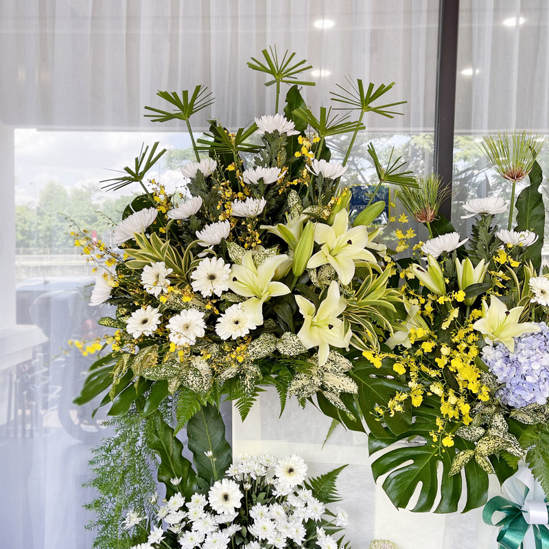 a large funeral flower stand arranged with white casablanca lilies, green chrysanthemums, and delicate pompom flowers in a structured stand