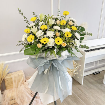 funeral flower wreath featuring yellow gerbera, white chrysanthemum, madonna lily and rose wrapped in soft blue and white fabric