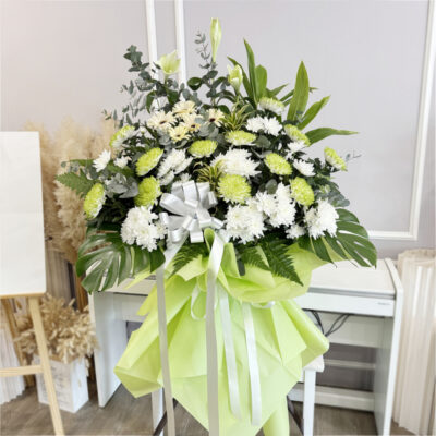 funeral flower stand featuring white gerbera, green chrysanthemum and madonna lily wrapped in light green paper with silver ribbon
