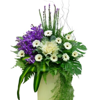 condolences flower stand featuring purple liatris, orchid, brassica and white gerbera with lush foliage in a tall arrangement
