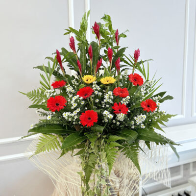 a vibrant opening flower stand with red ginger spikes, bright sunflowers and red gerbera surrounded by lush greenery