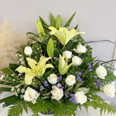 funeral basket featuring white roses, conca d'or lilies, and mixed greenery with subtle purple flowers.