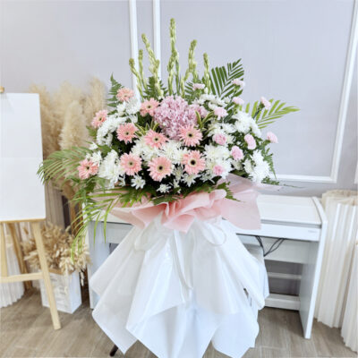 funeral flower stand with pink gerberas, white chrysanthemum pompoms, hydrangeas and tuberoses wrapped in soft pink and white paper