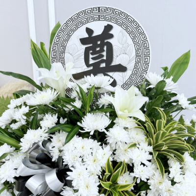 a solemn condolences flower stand arranged with white chrysanthemum and madonna lily wrapped in black plastic