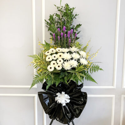 flower stand with white gerbera, white chrysanthemum, purple liatris, and yellow dancing lady flowers wrapped in black plastic with white ribbon