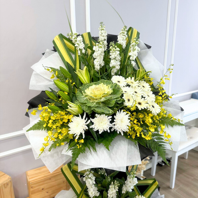 a floral stand featuring white chrysanthemums, white gerberas and green brassica wrapped in black and white paper