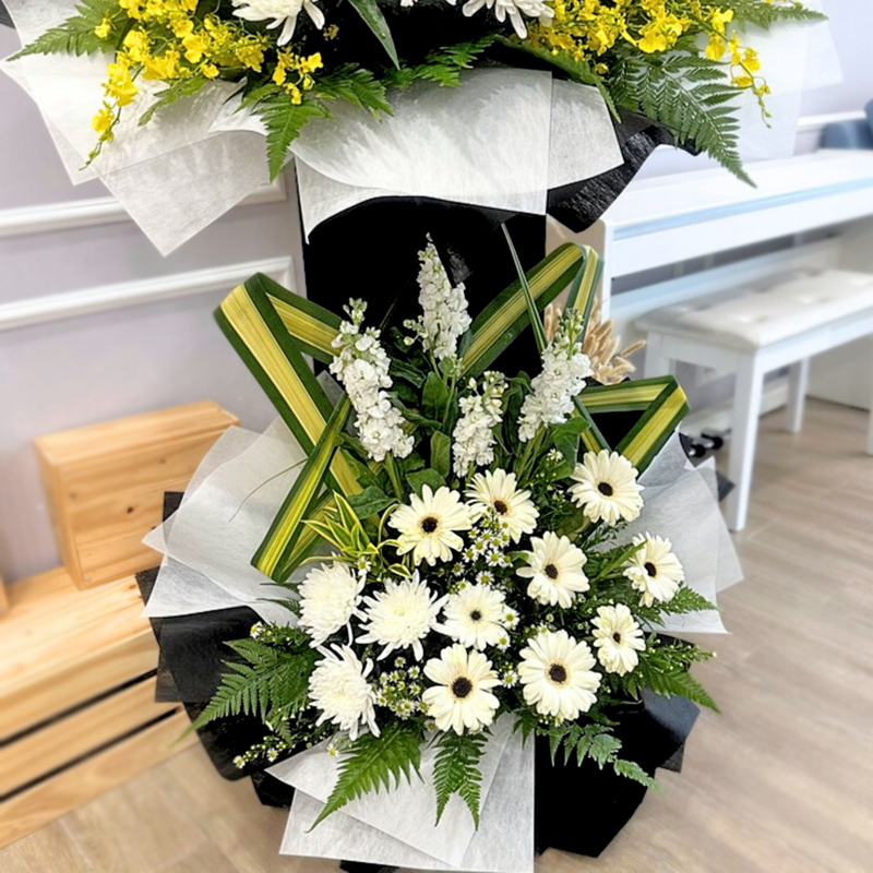 double-tiered condolences stand with white flowers including matthiola and gerbera accented with green leaves and yellow dancing lady