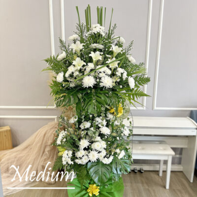 white chrysanthemum pompoms and madonna lilies arrangement on a funeral stand with lush green leaves