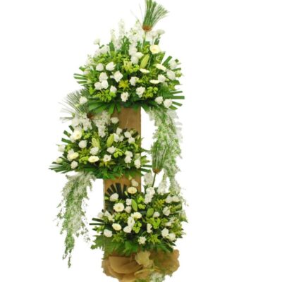 funeral flower stand featuring white matthiola, eustoma, lily, gerbera, and green chrysanthemum pompoms arranged in three tiers with natural foliage.