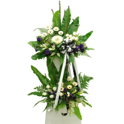 tall flower stand with white casablanca lily, white rose, purple eustoma, and lush green leaves arranged for a funeral tribute.