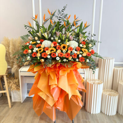 opening flower stand featuring bird of paradise, pink stargazer lily, sunflowers and white hydrangea wrapped in layered orange paper.