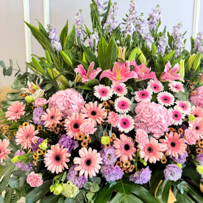 a tall congratulation flower stand featuring pink carnations, peach chrysanthemum pompoms and pink hydrangea with lush greenery