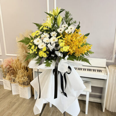 funeral flower stand with white gerbera, yellow chrysanthemum pompom, orange orchid and conca d'or lily wrapped in white and black ribbons