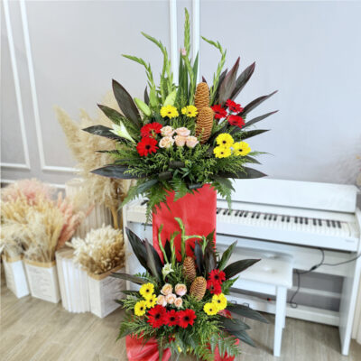 opening flower stand featuring peach gladiolus, pink rose, red and yellow gerbera with lush greenery wrapped in red wrapper