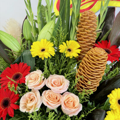 a tall congratulations flower stand with yellow gerbera, red gerbera, peach gladiolus, pink rose and green foliage in a red wrapper