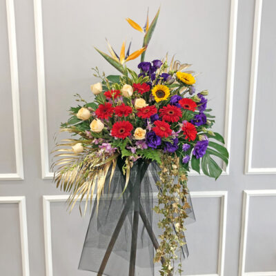 opening flower stand with bird of paradise, champagne roses, red gerberas, orchids, sunflowers and purple eustomas in a tall arrangement