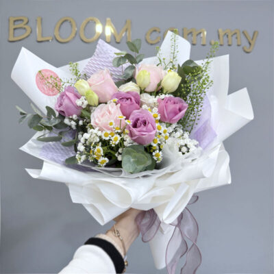 a flower bouquet featuring purple and pink roses with white eustoma, chamomile, and babyโs breath wrapped in white paper