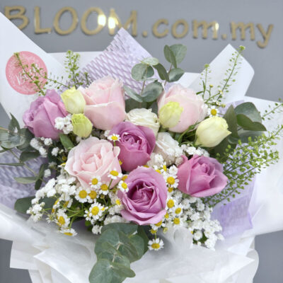 bouquet of mixed purple and pink roses accented with white eustoma, chamomile flowers, and greenery in delicate wrapping