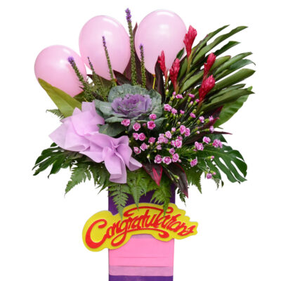 congratulation flower stand featuring red ginger, pink carnation spray, brassica, liatris and pink balloons with lush greenery in a congratulatory arrangement.