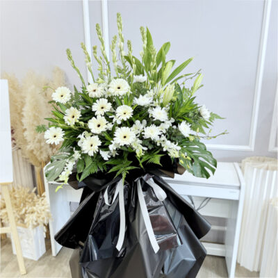 flower stand of condolences with white gerbera, chrysanthemum pompoms, orchid and tuberosa arranged on a tall wooden stand wrapped in black