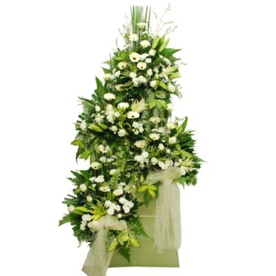 funeral flower stand featuring white casablanca lilies, white gerberas, white roses, and white chrysanthemum pompom arranged with lush green foliage