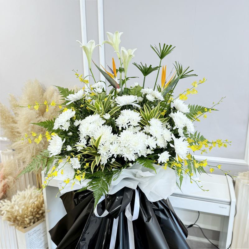funeral stand bouquet with mixed white flowers including chrysanthemum and madonna lily, accented with bird of paradise and dancing lady
