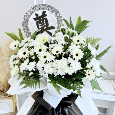 flower stand of funeral featuring casablanca lily, white chrysanthemum pompoms and white gerbera with green foliage wrapped in white and black