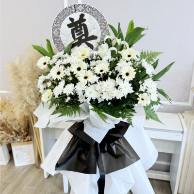 a tall condolences flower stand with white casablanca lily and chrysanthemum pompoms accented by white gerbera and lush greenery