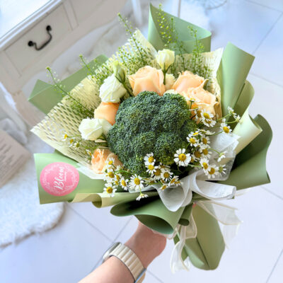 a flower bouquet featuring broccoli flowers, champagne colour roses, white eustoma, and chamomile wrapped in green and cream paper