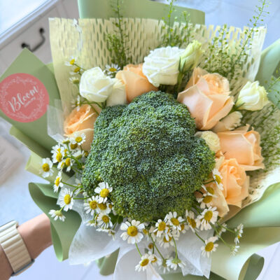 hand bouquet with broccoli flowers, champagne colour roses, white eustoma, and chamomile arranged in layered green wrapping