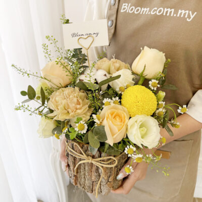 flower arrangement in a rustic bark barrel bucket featuring champagne roses, white eustoma, carnation, and yellow chrysanthemum ping pong