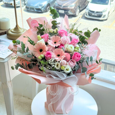 flower bouquet wrapped in soft pink paper featuring pink roses, pink gerbera, white eustoma, pink chrysanthemum pingpong flowers and pink feathers