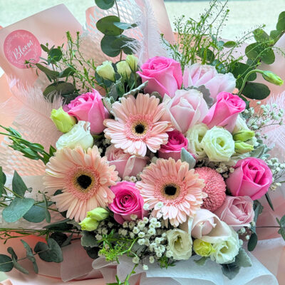 a bouquet of mixed pink flowers including hot pink roses, pink gerbera, white eustoma and delicate pink feathers in soft pastel wrapping