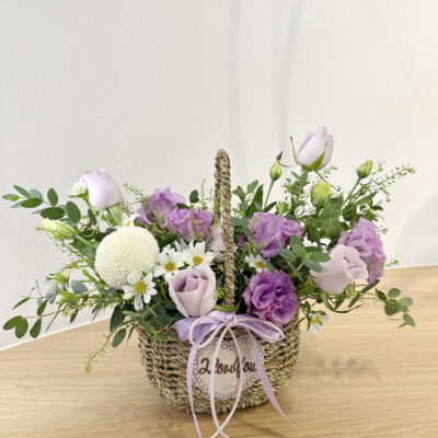 flower arrangement in a woven basket featuring lilac rose, purple eustoma, white chrysanthemum ping pong and white hana flower